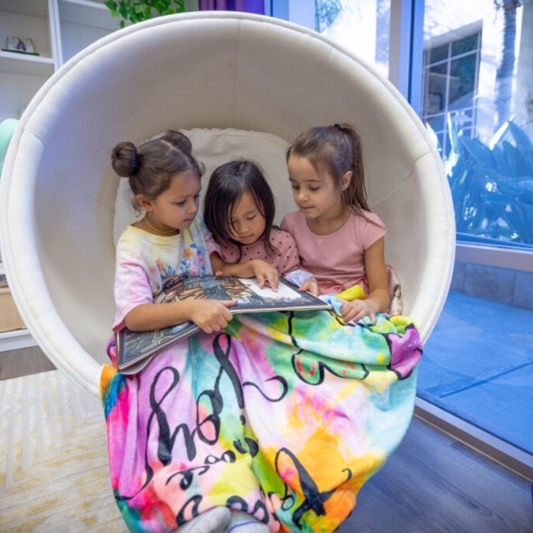 An image of three little girls reading in a chair.